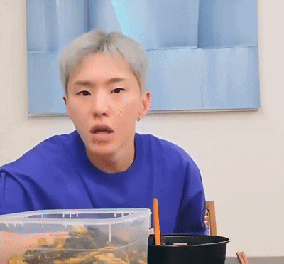 A Man In A Blue Shirt Is Sitting At A Table With A Bowl Of Food And Chopsticks GIF