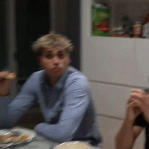 A Man In A Blue Shirt Is Sitting At A Table With A Plate Of Food . GIF