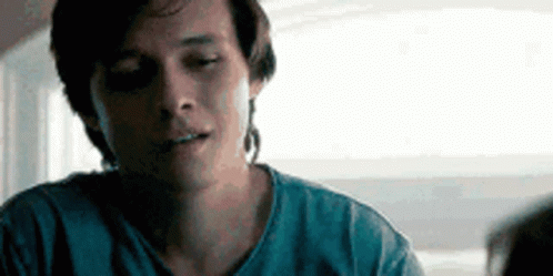 A Man In A Blue Shirt Is Sitting At A Table With His Eyes Closed And Looking At Something . GIF