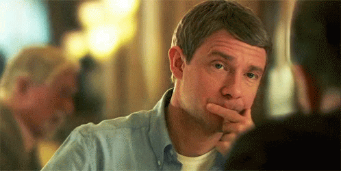 A Man In A Blue Shirt Is Sitting At A Table With His Hand To His Chin . GIF