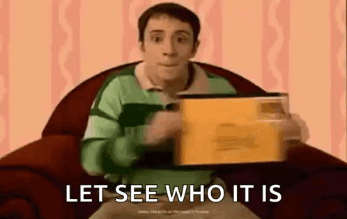 A Man In A Blue Shirt Is Sitting In A Chair Holding A Box And Saying `` Let See Who It Is `` . GIF