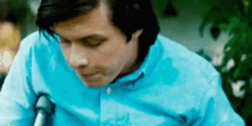 A Man In A Blue Shirt Is Sitting In A Chair . GIF
