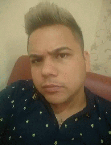 A Man In A Blue Shirt Is Sitting In A Chair Making A Funny Face GIF