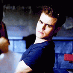 A Man In A Blue Shirt Is Sitting In A Dark Room . GIF