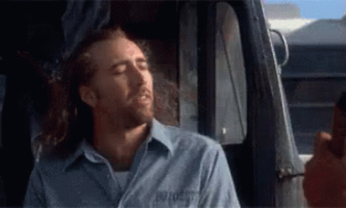A Man In A Blue Shirt Is Sitting In A Truck Smoking A Cigarette . GIF