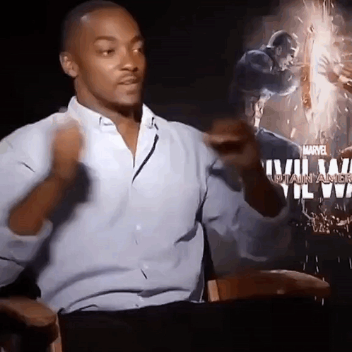 A Man In A Blue Shirt Is Sitting In Front Of A Poster For Captain America . GIF