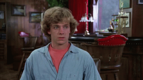 A Man In A Blue Shirt Is Sitting In Front Of A Red Chair GIF