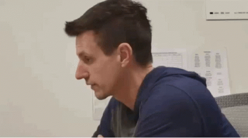 a man in a blue shirt is sitting in front of a white wall with papers on it
