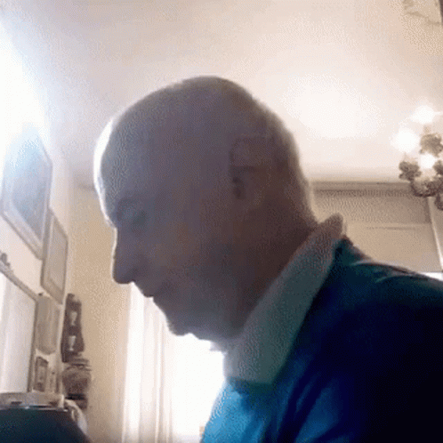 A Man In A Blue Shirt Is Sitting In Front Of A Window . GIF