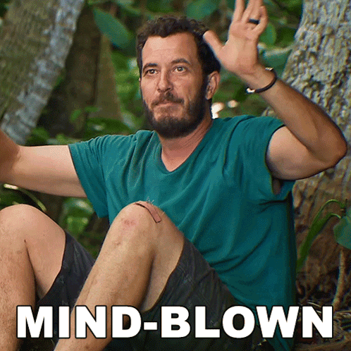 A Man In A Blue Shirt Is Sitting In The Woods With The Words Mind-Blown Behind Him GIF
