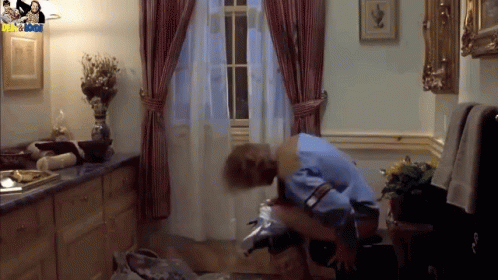 A Man In A Blue Shirt Is Sitting On A Chair In A Room With A Picture Of A Man And A Woman On The Wall GIF