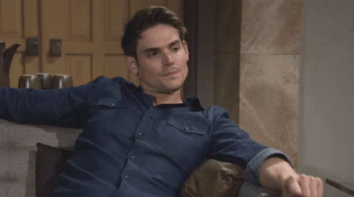 A Man In A Blue Shirt Is Sitting On A Chair GIF