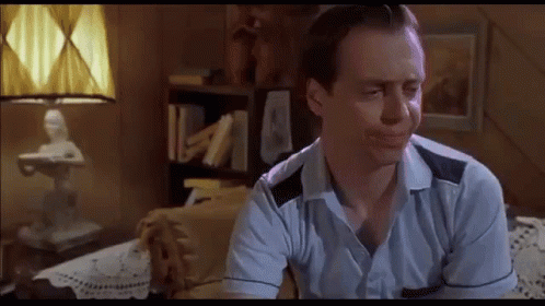 A Man In A Blue Shirt Is Sitting On A Couch In A Living Room . GIF
