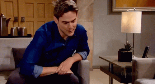 A Man In A Blue Shirt Is Sitting On A Couch In Front Of A Lamp That Says Global GIF