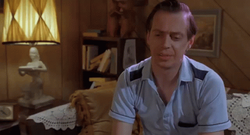 A Man In A Blue Shirt Is Sitting On A Couch In Front Of A Lamp GIF