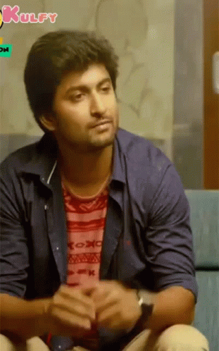 A Man In A Blue Shirt Is Sitting On A Couch With A Kulfy Logo In The Background GIF