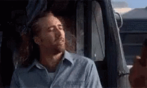 A Man In A Blue Shirt Is Sleeping In A Truck . GIF