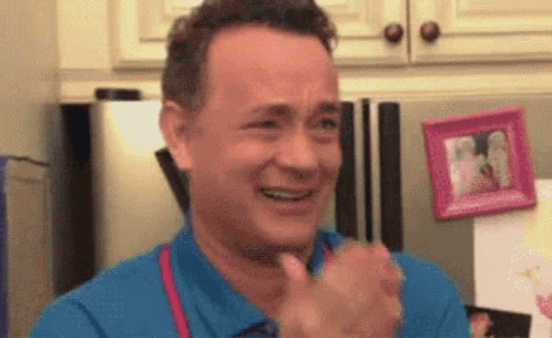 A Man In A Blue Shirt Is Smiling And Clapping His Hands In Front Of A Refrigerator . GIF