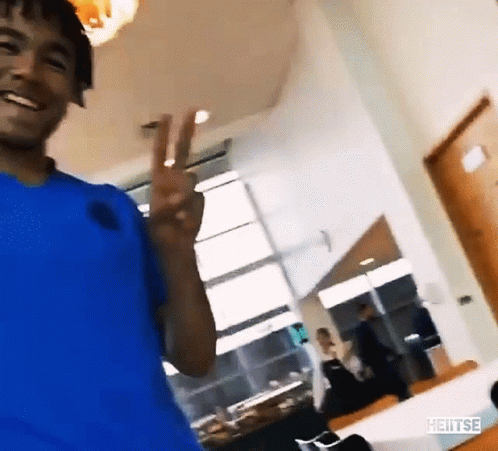 A Man In A Blue Shirt Is Smiling And Giving A Peace Sign GIF