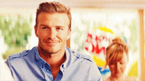 A Man In A Blue Shirt Is Smiling And Looking At The Camera GIF