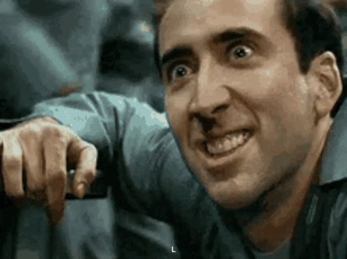 A Man In A Blue Shirt Is Smiling And Pointing At Something . GIF