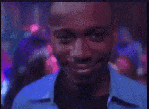A Man In A Blue Shirt Is Smiling In A Club GIF