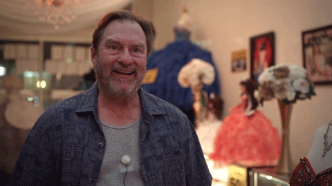 a man in a blue shirt is smiling in front of a sign that says ' a ' on it