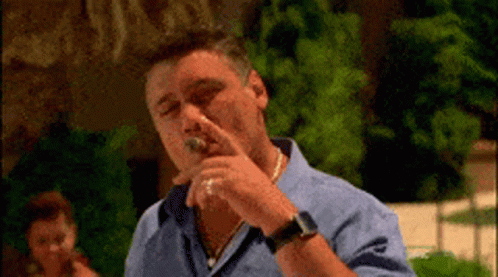 A Man In A Blue Shirt Is Smoking A Cigar Outdoors GIF