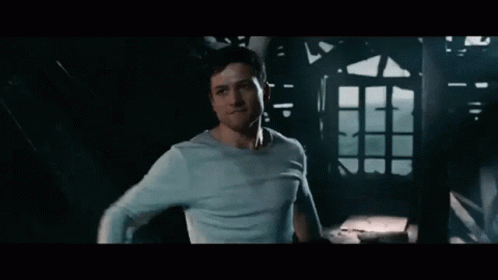 A Man In A Blue Shirt Is Standing In A Dark Room Looking At Something . GIF