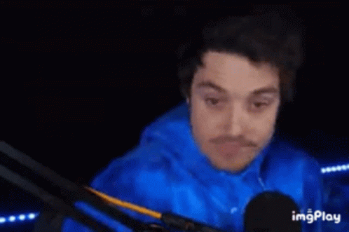 A Man In A Blue Shirt Is Standing In A Dark Room With His Hands Behind His Back . GIF