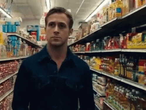 A Man In A Blue Shirt Is Standing In A Grocery Store Aisle Looking At Something GIF