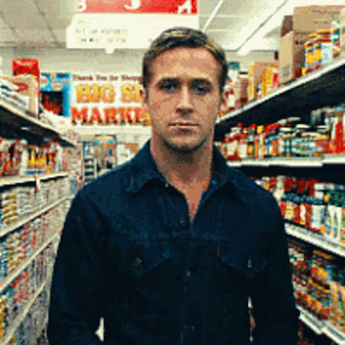 A Man In A Blue Shirt Is Standing In A Grocery Store With A Sign That Says Big Sale Market GIF