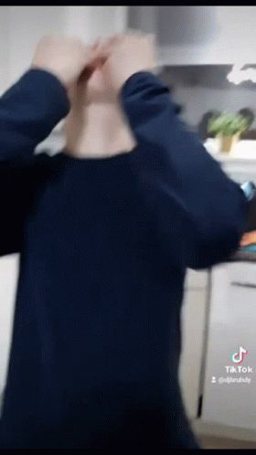 A Man In A Blue Shirt Is Standing In A Kitchen With His Hands On His Head GIF
