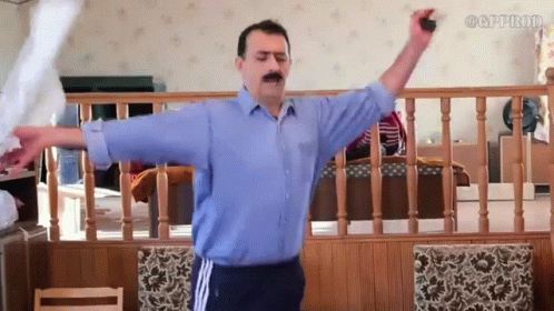 A Man In A Blue Shirt Is Standing In A Living Room With His Arms Outstretched .. GIF