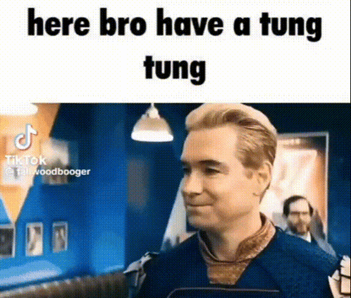 A Man In A Blue Shirt Is Standing In A Room With A Sign That Says `` Here Bro Have A Tung Tung '' . GIF