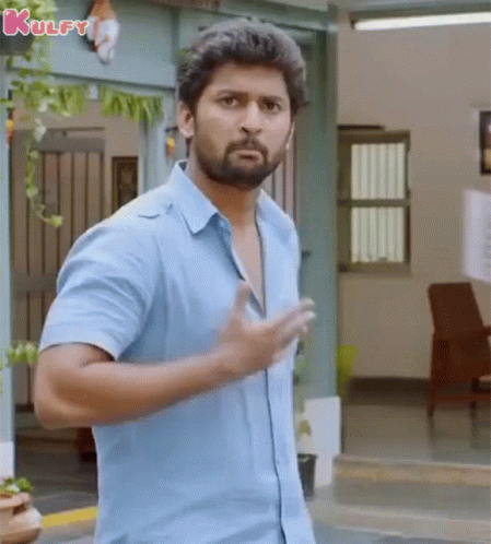 A Man In A Blue Shirt Is Standing In Front Of A Building And Making A Funny Face . GIF