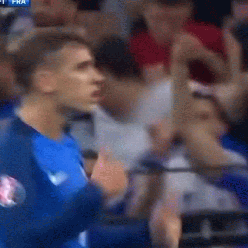 A Man In A Blue Shirt Is Standing In Front Of A Crowd GIF