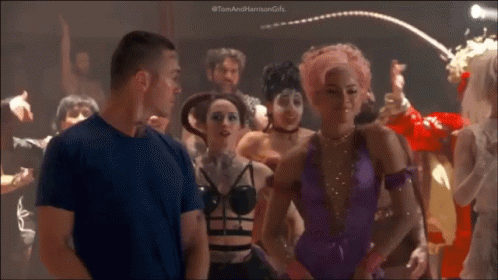 A Man In A Blue Shirt Is Standing In Front Of A Crowd Of People Dancing In A Club . GIF