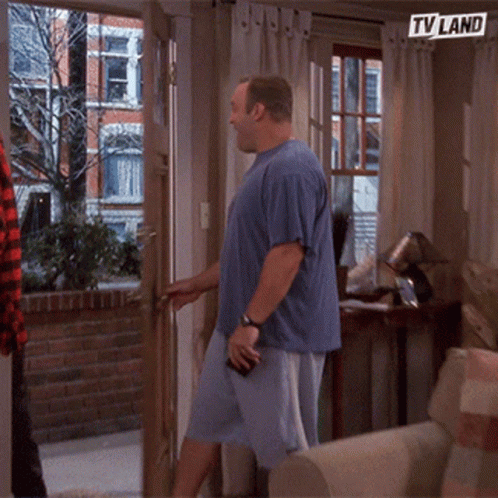 A Man In A Blue Shirt Is Standing In Front Of A Door With A Tv Land Sign Above Him GIF