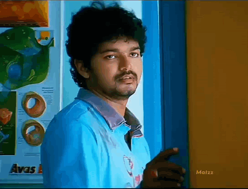 A Man In A Blue Shirt Is Standing In Front Of A Door With The Word Avas On It GIF