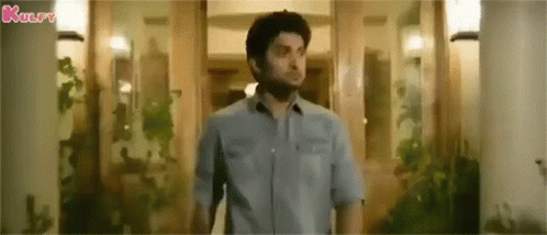 A Man In A Blue Shirt Is Standing In Front Of A Doorway In A Room . GIF