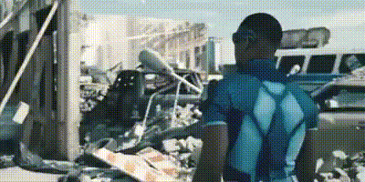 A Man In A Blue Shirt Is Standing In Front Of A Pile Of Rubble In A Parking Lot . GIF
