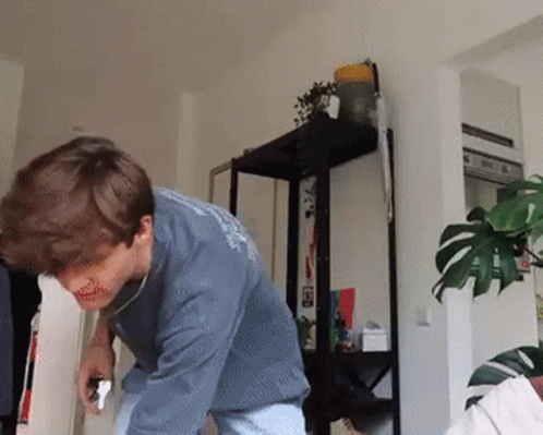 A Man In A Blue Shirt Is Standing In Front Of A Plant GIF