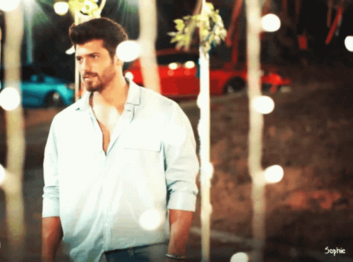 A Man In A Blue Shirt Is Standing In Front Of A Red Car And Trees GIF