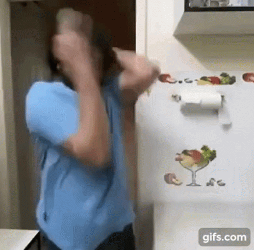 A Man In A Blue Shirt Is Standing In Front Of A Refrigerator With A Paper Towel Holder On It . GIF