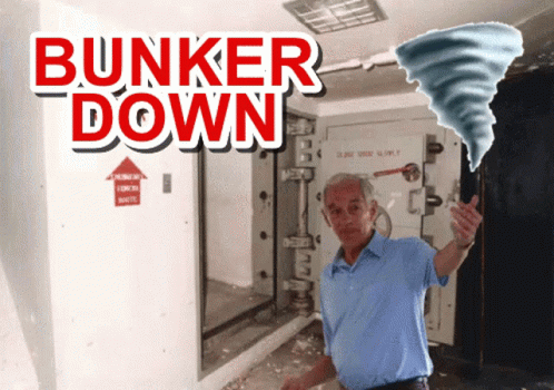 A Man In A Blue Shirt Is Standing In Front Of A Sign That Says " Bunker Down " GIF