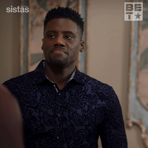 A Man In A Blue Shirt Is Standing In Front Of A Wall With A Sistas Logo On It GIF