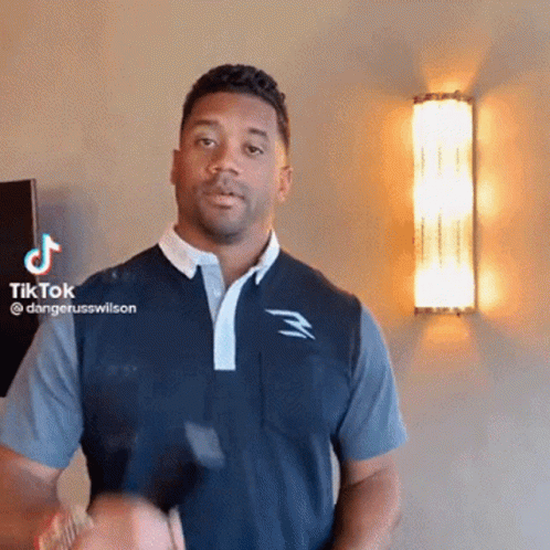 A Man In A Blue Shirt Is Standing In Front Of A Wall With A Tiktok Logo On It . GIF