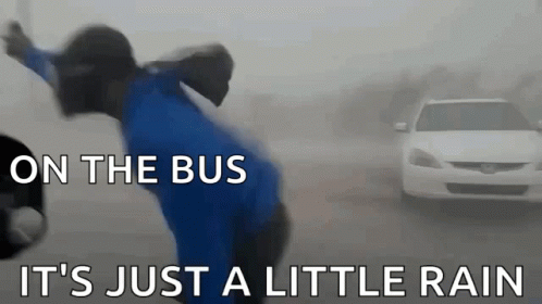 A Man In A Blue Shirt Is Standing In Front Of A White Car With The Words On The Bus It 'S Just A Little Rain GIF