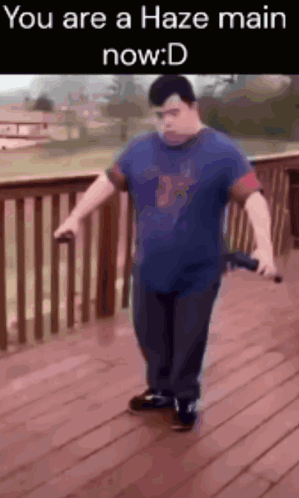 A Man In A Blue Shirt Is Standing On A Wooden Deck Holding A Sword And A Microphone .. GIF